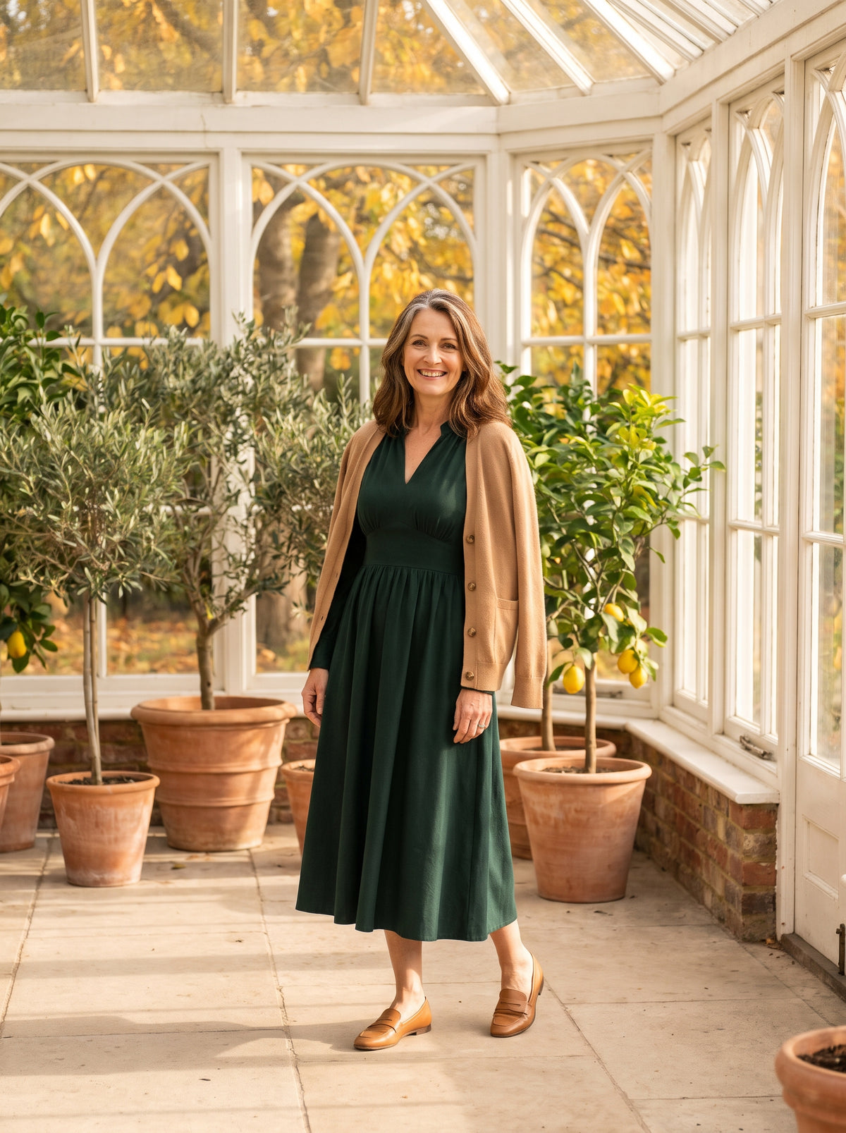 Woman in a green midi dress and camel cardigan in a sunlit orangery